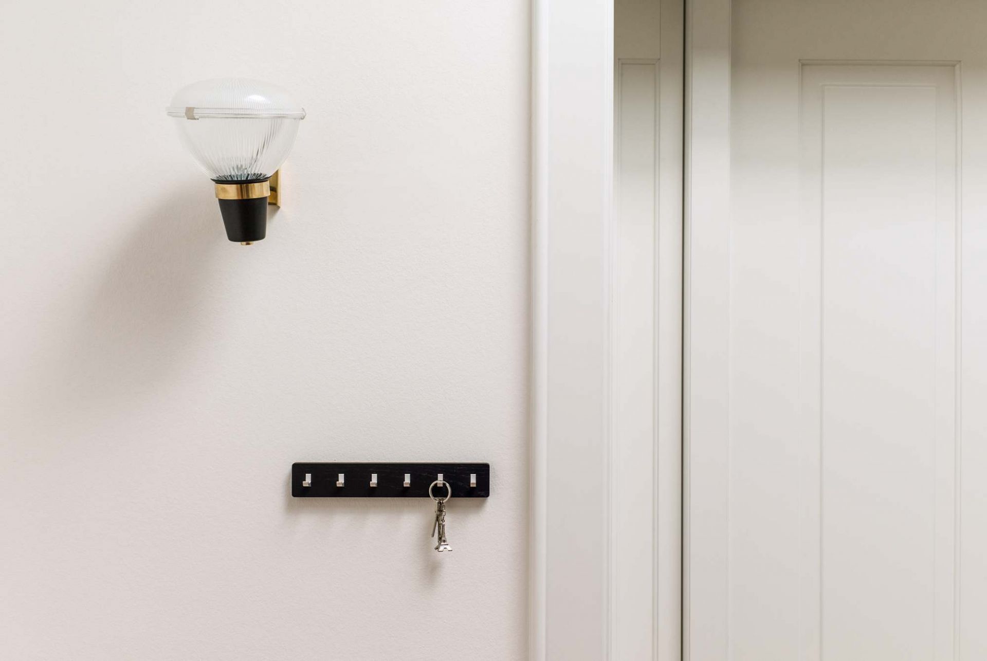 Schwarze Schönbuch Key Bar Schlüsselhakenleiste an der Wand mit Schlüssel, neben einer Lampe und Tür.