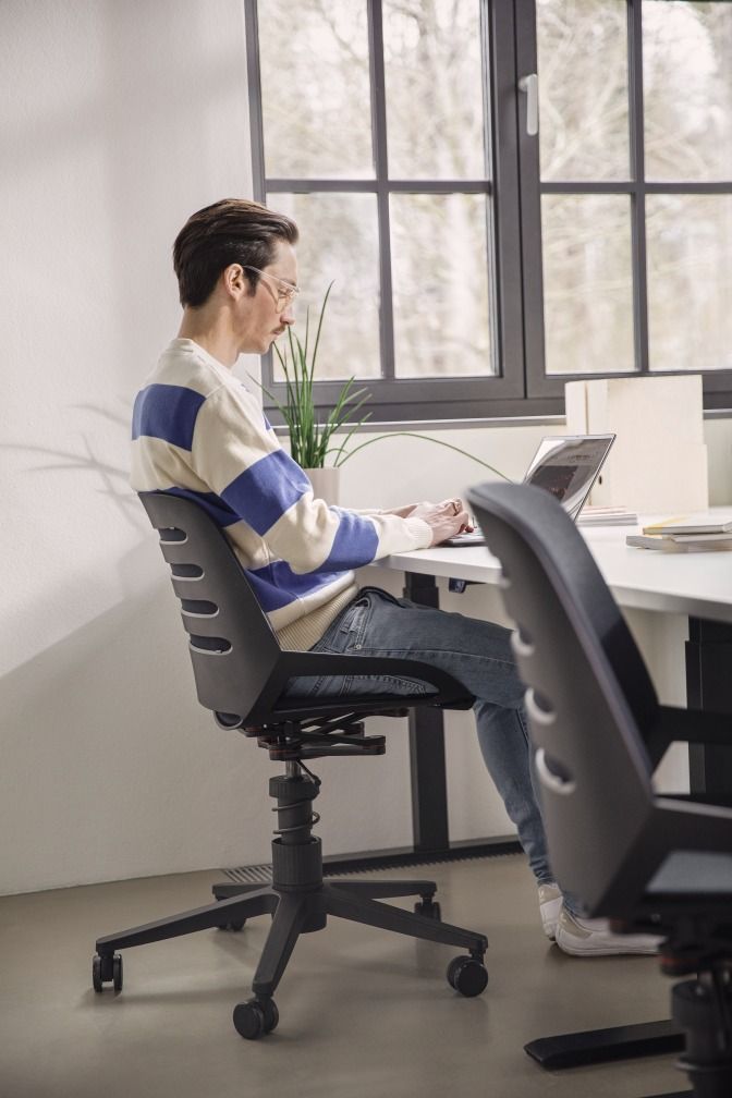 Mann sitzt auf einem Numo Bürodrehstuhl von Aeris mit Federbein und Rollen vor einem Laptop.