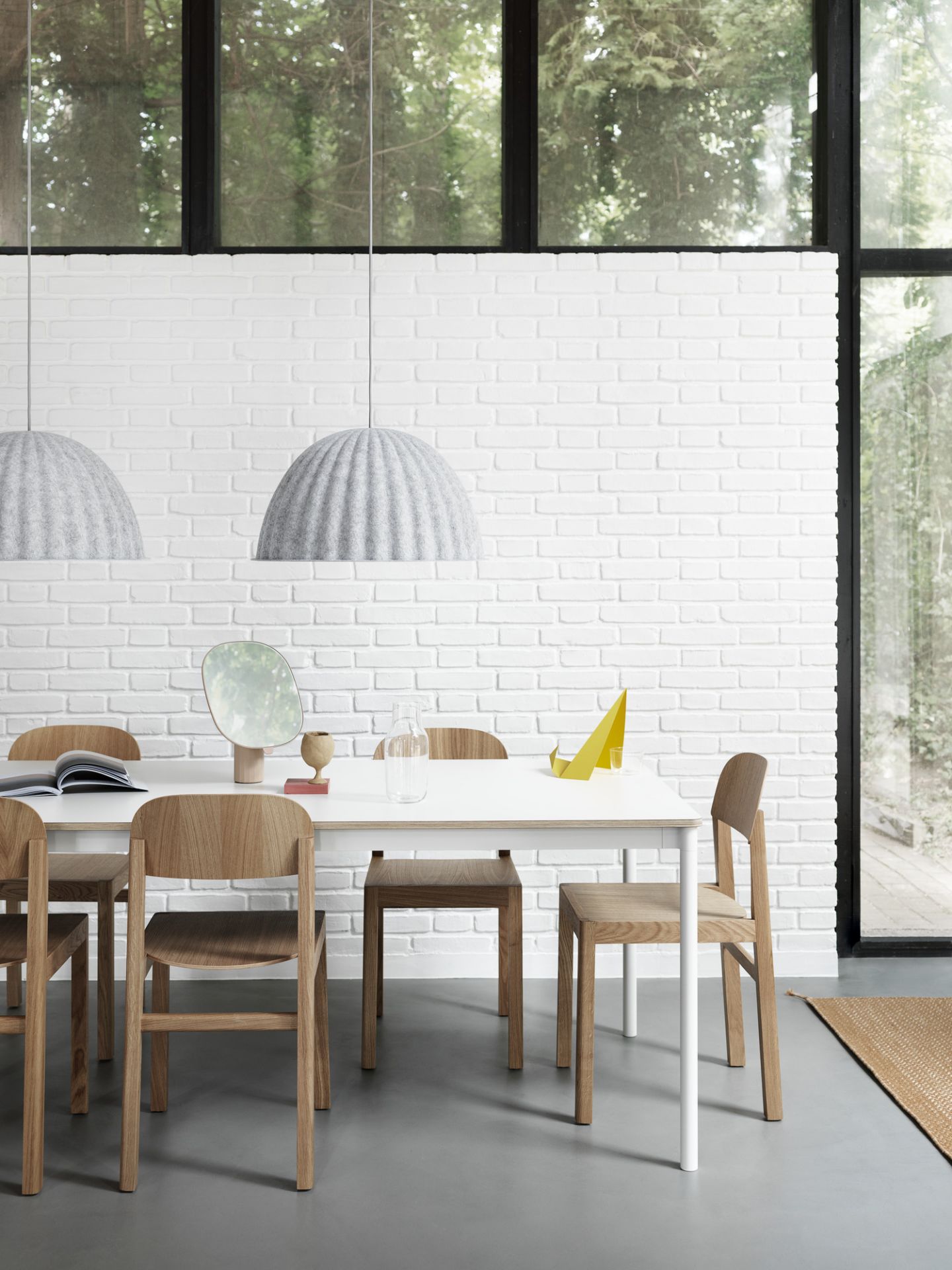 Heller Essbereich mit Muuto Base Table Tisch, Holzstühlen, grauen Lampen und weißen Ziegelwänden.