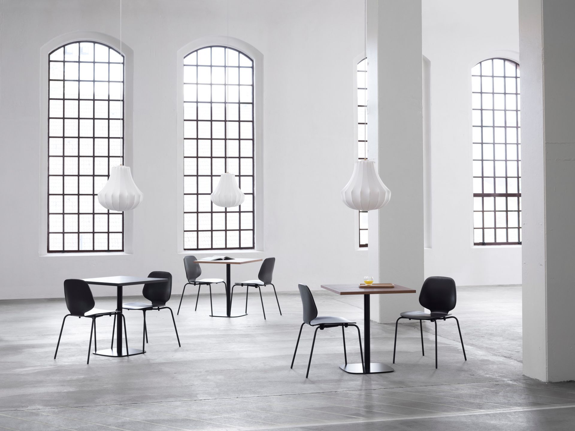 Innenaufnahme mit drei großen, weißen Phantom Pendelleuchten von Normann Copenhagen über Tischen.