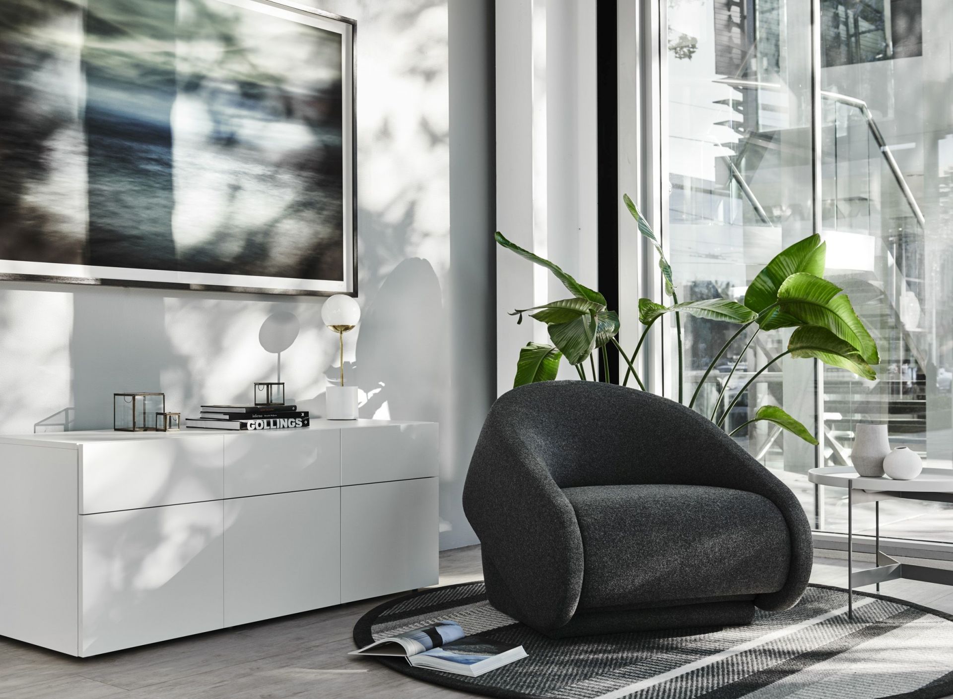 Grauer Up-lift Sessel von Prostoria im modernen Wohnzimmer mit weißem Sideboard und Fensterfront.