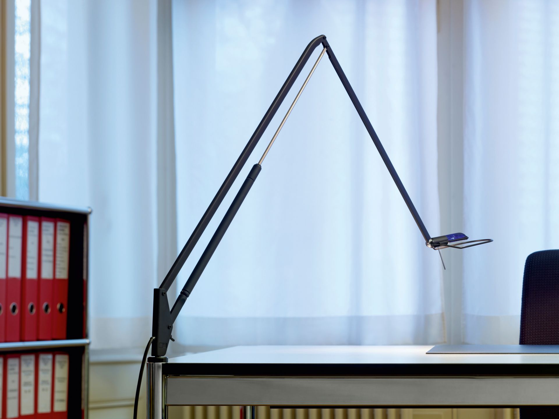 Schwarze Lifto LED Tischleuchte von Belux auf einem Schreibtisch vor einem Fenster. Dimmbare Büroleuchte.