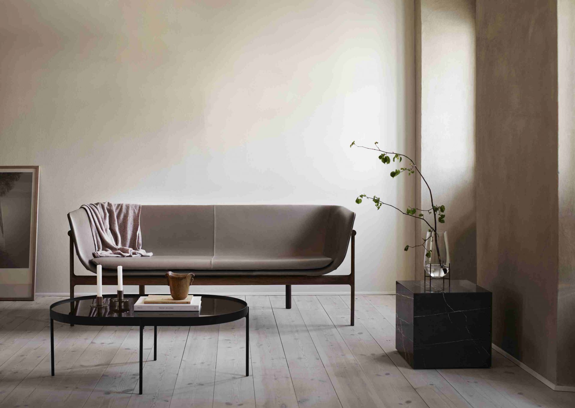 Audo Copenhagen Plinth Tisch aus Marmor, runder Couchtisch und graues Sofa im minimalistischen Wohnzimmer.