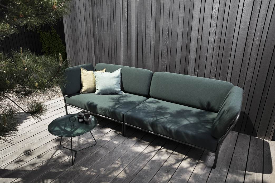 Houe Level Outdoor Sofa Ecke links mit Kissen und kleinem Tisch auf Holzterrasse.