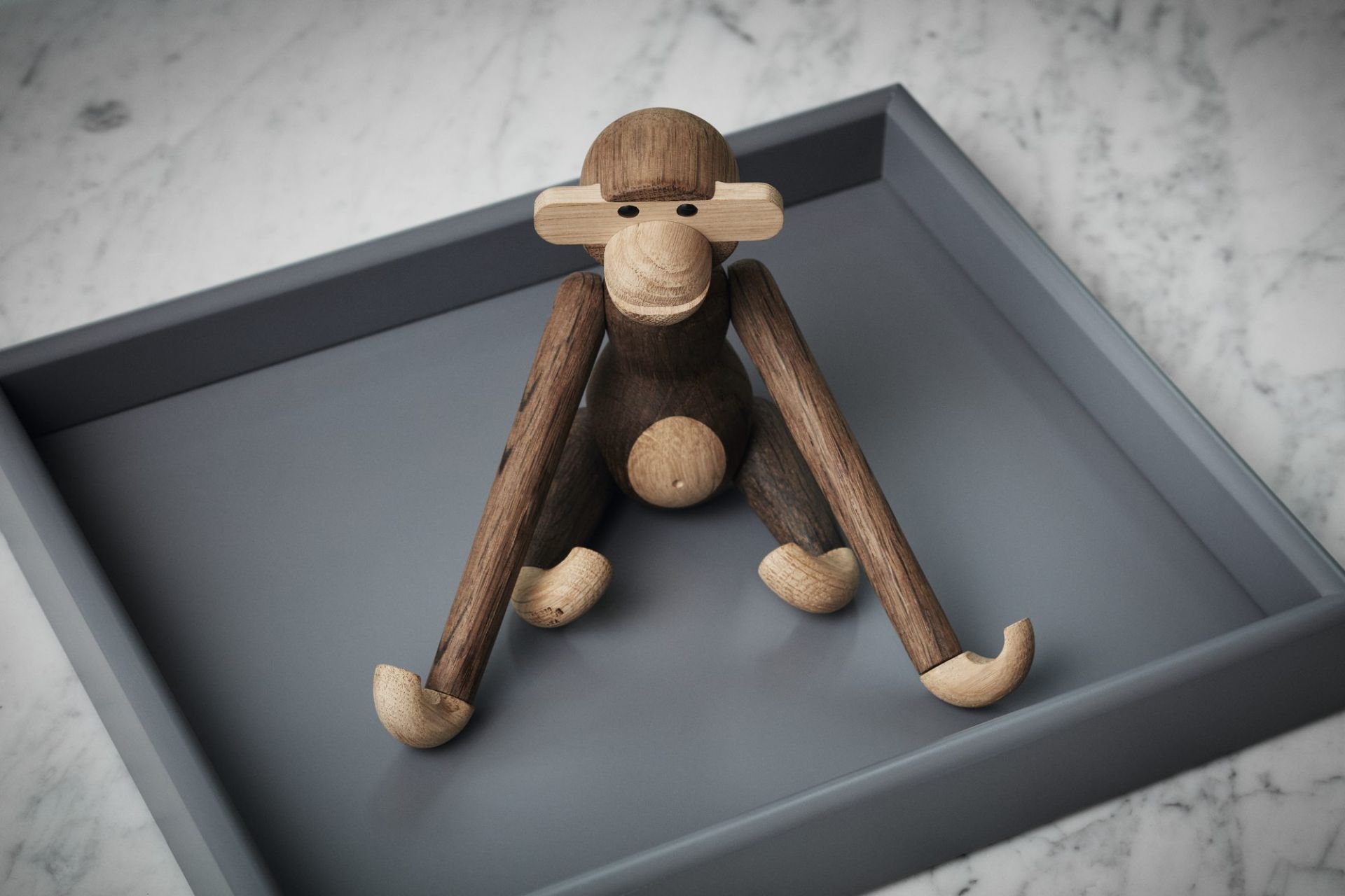 Affe Holzfigur, geräucherte Eiche, von Kay Bojesen, sitzend auf einem grauen Tablett.