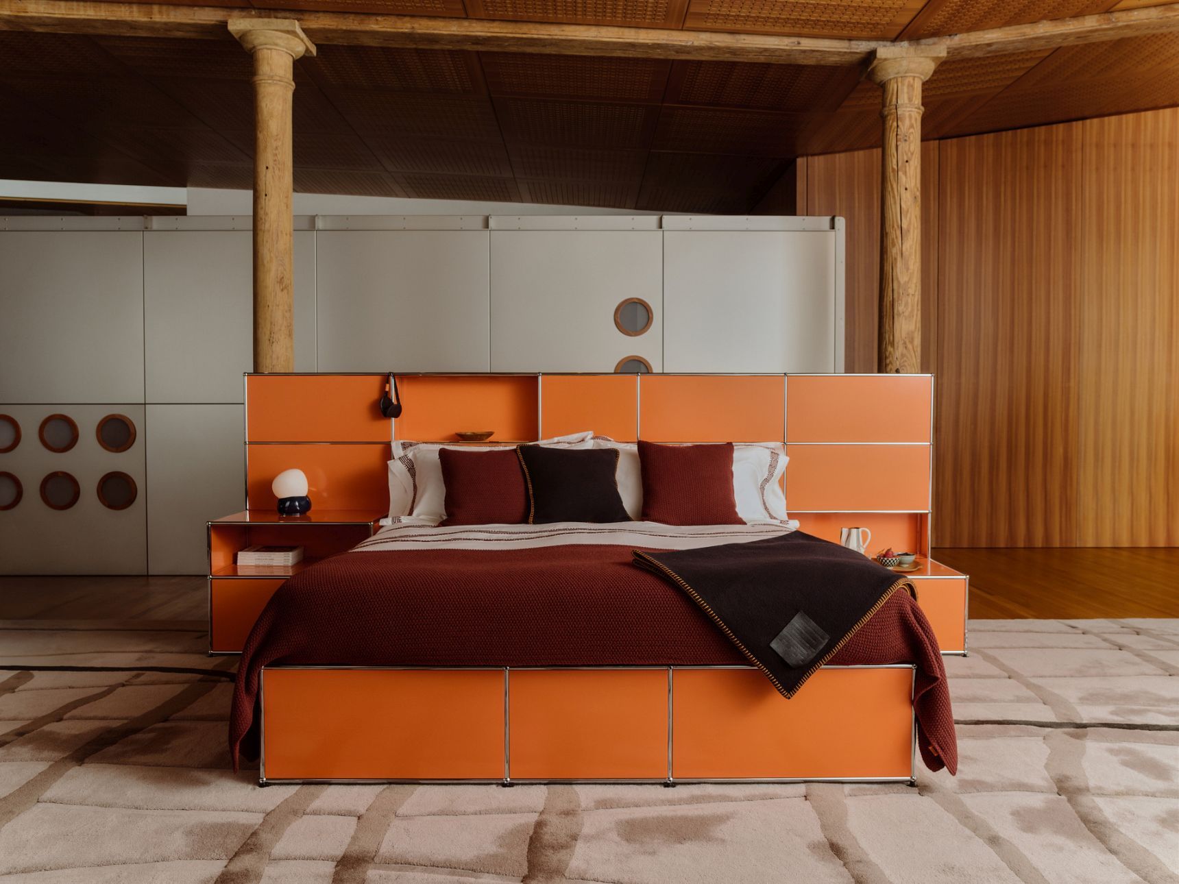 USM Haller Bett Mansa in Orange mit Nachttisch und brauner Tagesdecke in Loft-Umgebung.