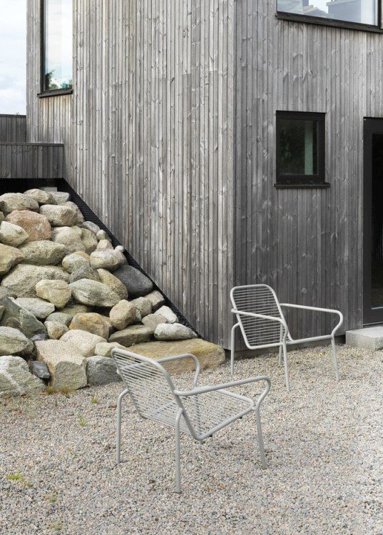 Zwei graue Vig Lounge Chairs von Normann Copenhagen im Außenbereich vor einem modernen Holzhaus.