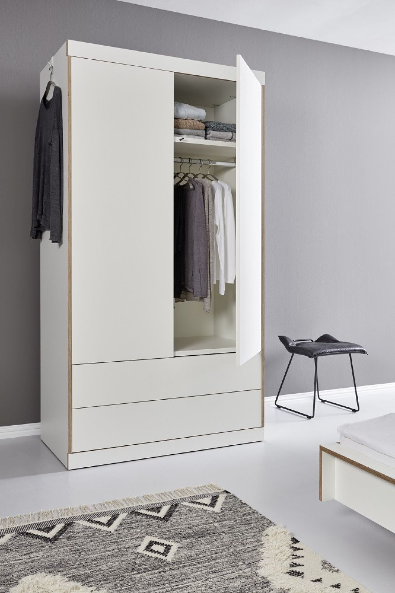 Flai Kleiderschrank von Müller Möbelwerkstätten mit zwei Türen, zwei Schubladen und Kleidung.