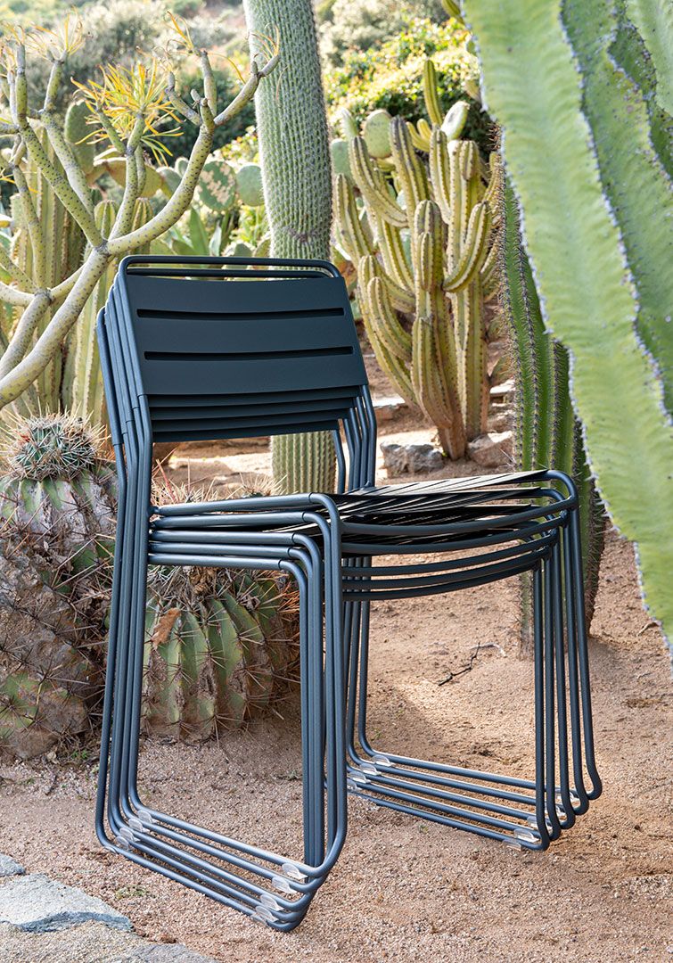 Stapel grauer Surprising Chair Stühle von Fermob für den Außenbereich vor Kakteen.