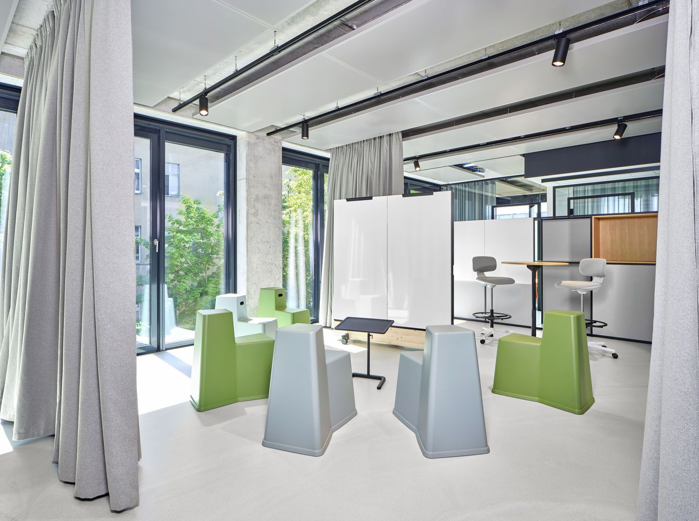 Modernes Büro mit Vitra Rookie High Drehstühlen in Grau und Grün, Besprechungstisch und Whiteboard.