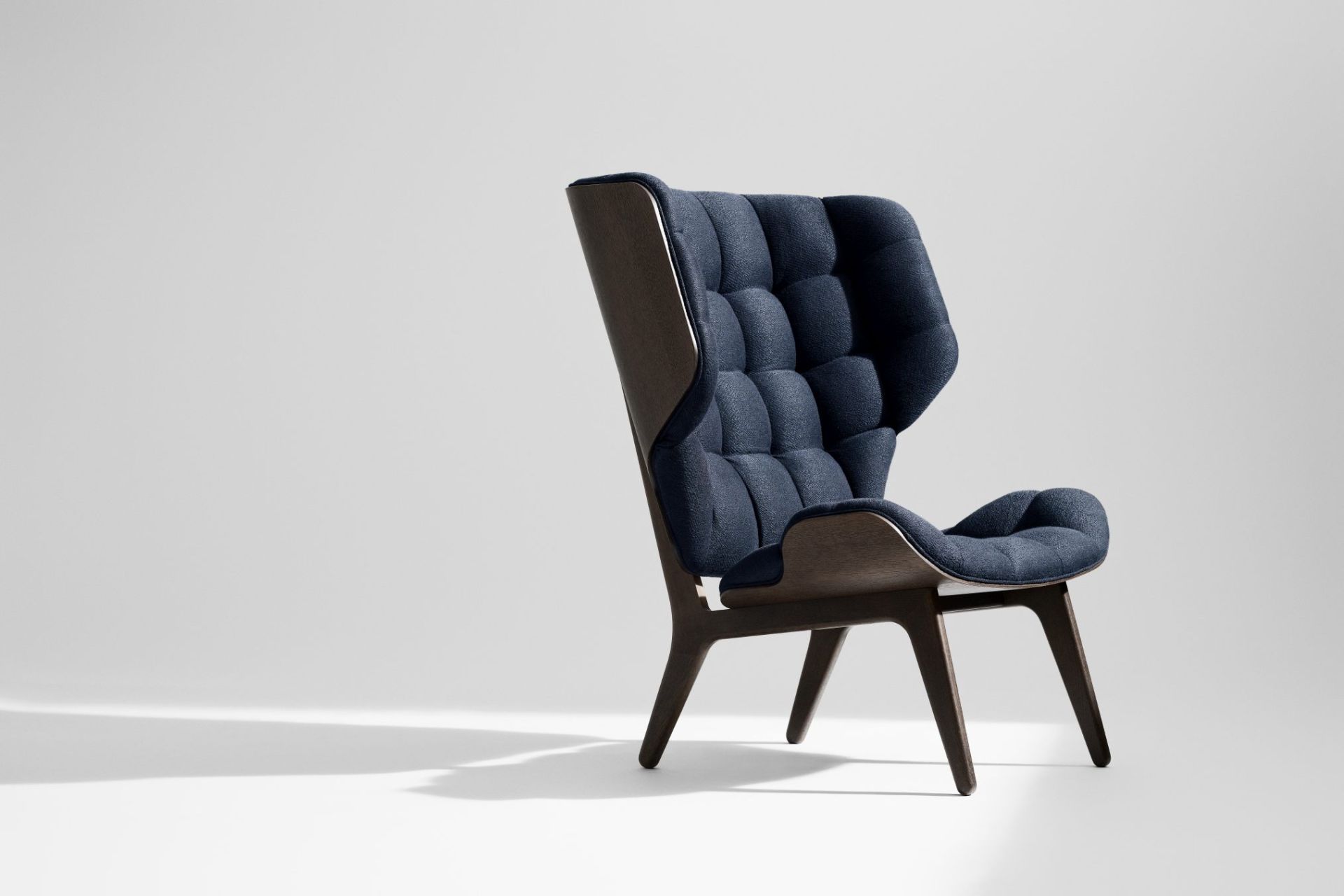 Mammoth Chair Sessel von NORR11 mit dunkelblauem Stoffbezug und dunklem Holzgestell auf weißem Hintergrund.