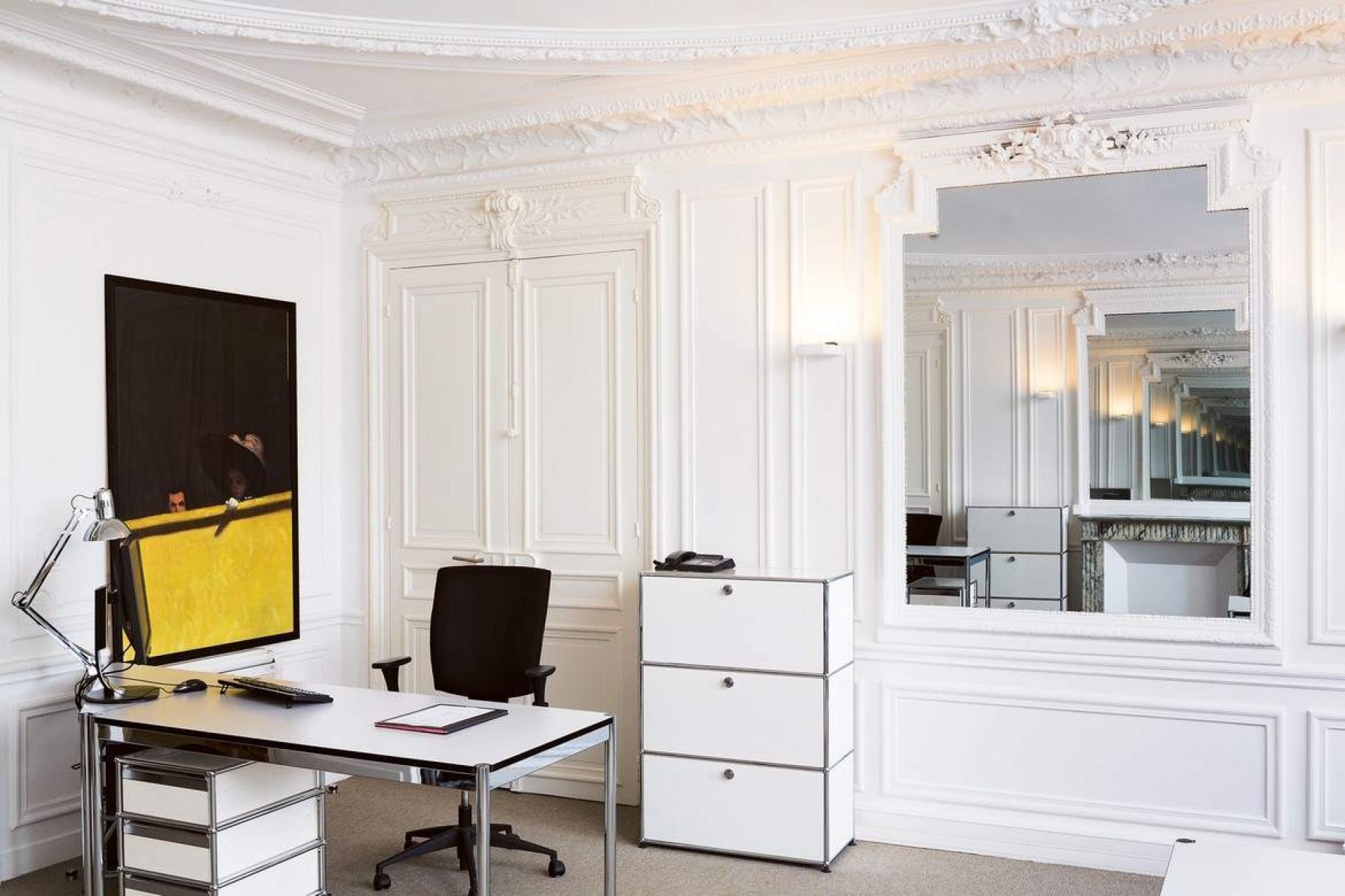 Weißer USM Haller Rollcontainer im Büro mit Schreibtisch, Stuhl und Kunstwerk.