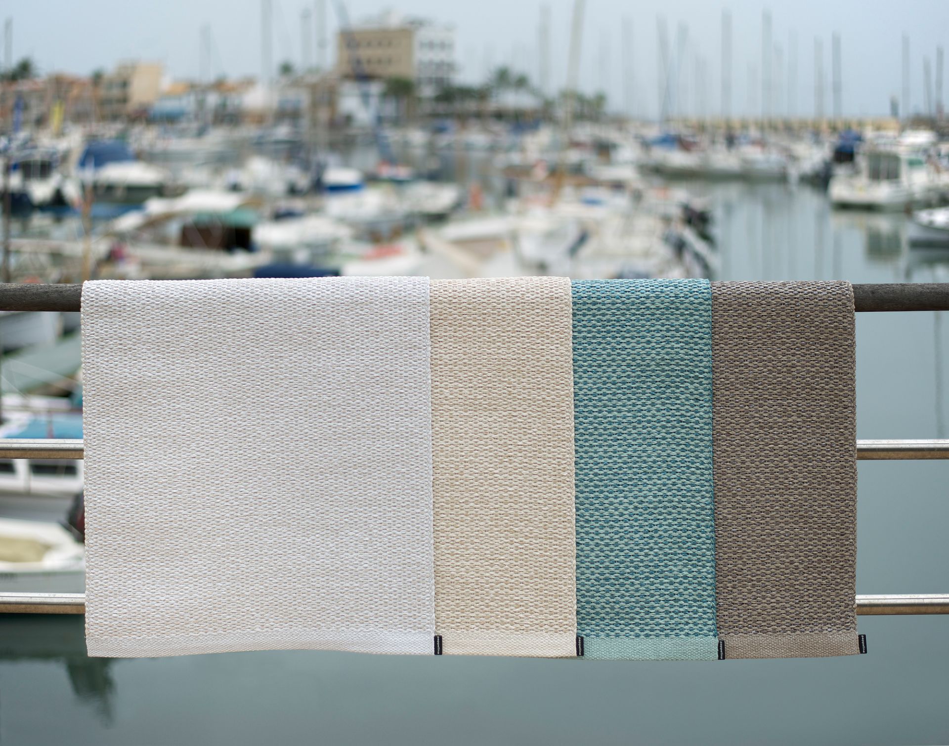 Svea Pappelina Kunststoffteppich in Weiß, Beige, Türkis und Braun vor einem Hafen mit Booten.