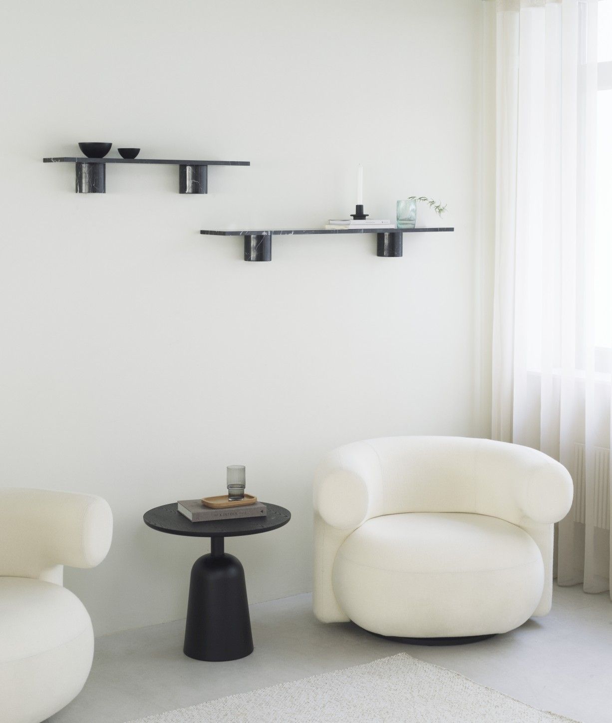 Zwei schwarze Sten Regale von Normann Copenhagen an einer weißen Wand, kombiniert mit minimalistischen Möbeln.