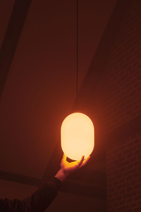 Nahaufnahme einer Hand, die eine leuchtende, graue Pendelleuchte hält. Moderne Lampe für Wohnzimmer und Esszimmer.