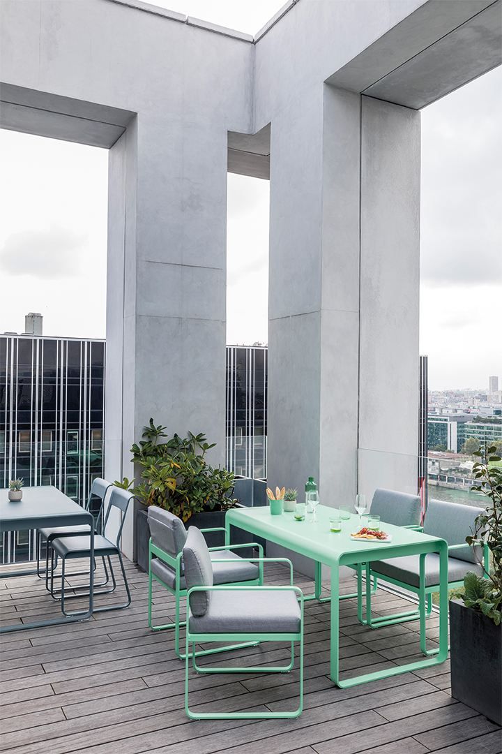 Bellevie Sessel Outdoor Fermob in Mintgrün mit Esstisch und Stühlen auf einer Dachterrasse.