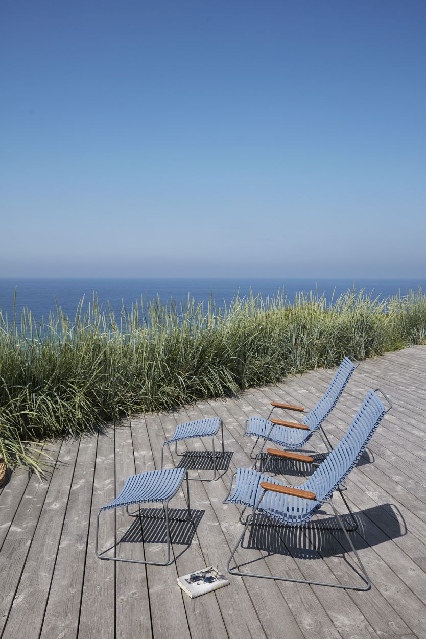 Houe Click Fußhocker und Gartenliegen in Blau auf Holzterrasse mit Meerblick, Outdoor Möbel.