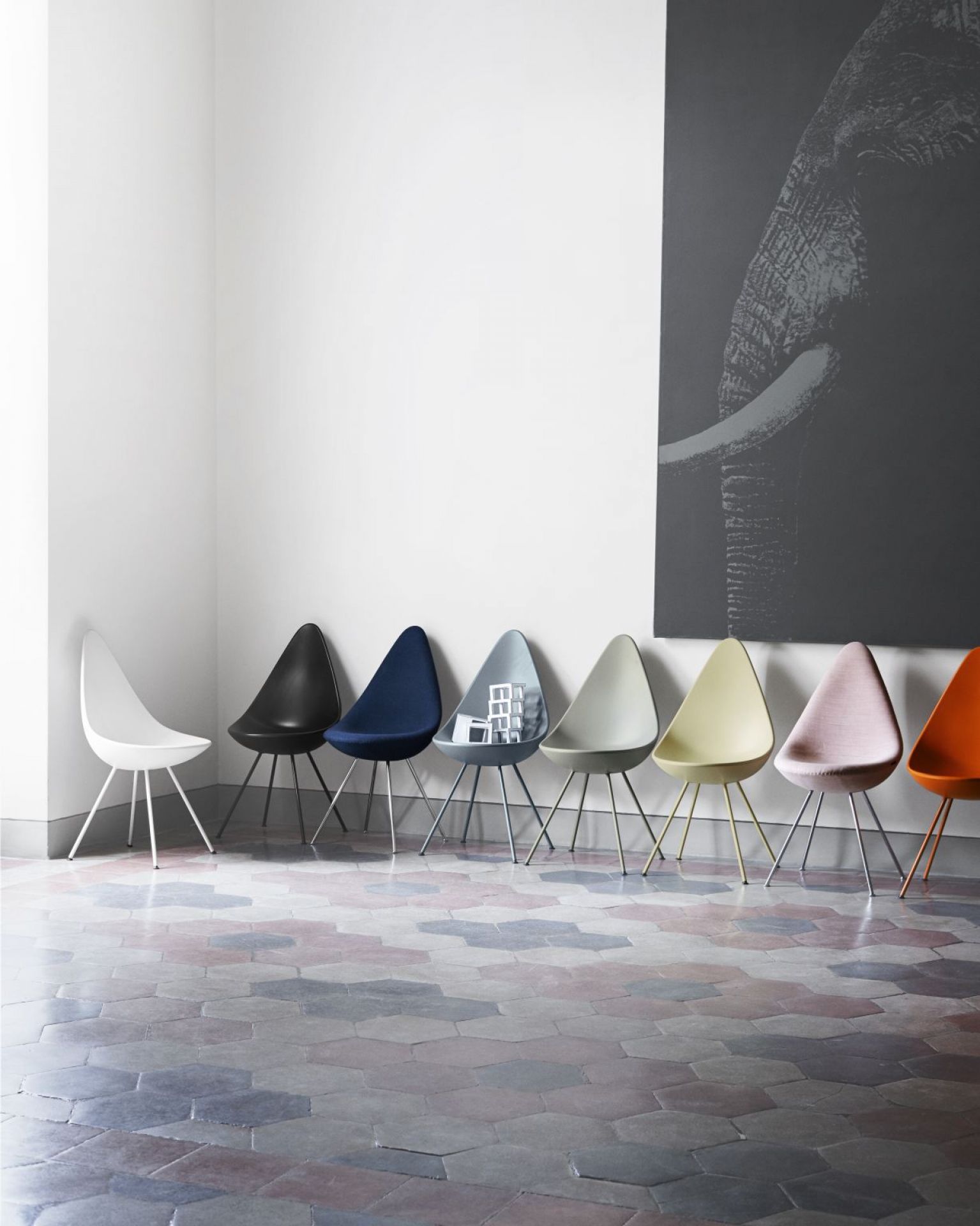 Reihe von Fritz Hansen Drop Stühlen in verschiedenen Farben vor einer Wand mit Elefantenbild.
