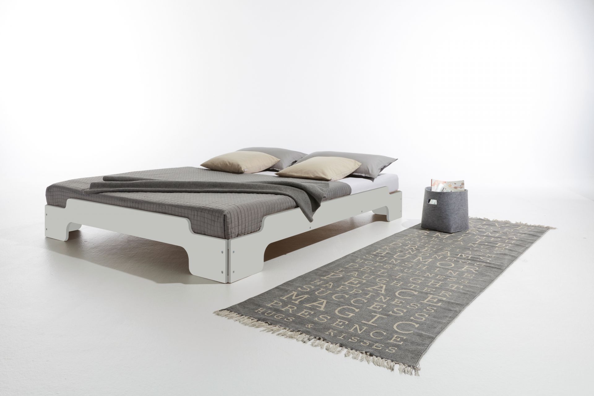 Weiße Stapelliege CPL von Müller Möbelwerkstätten mit grauer Tagesdecke, Kissen und Teppich im Schlafzimmer.