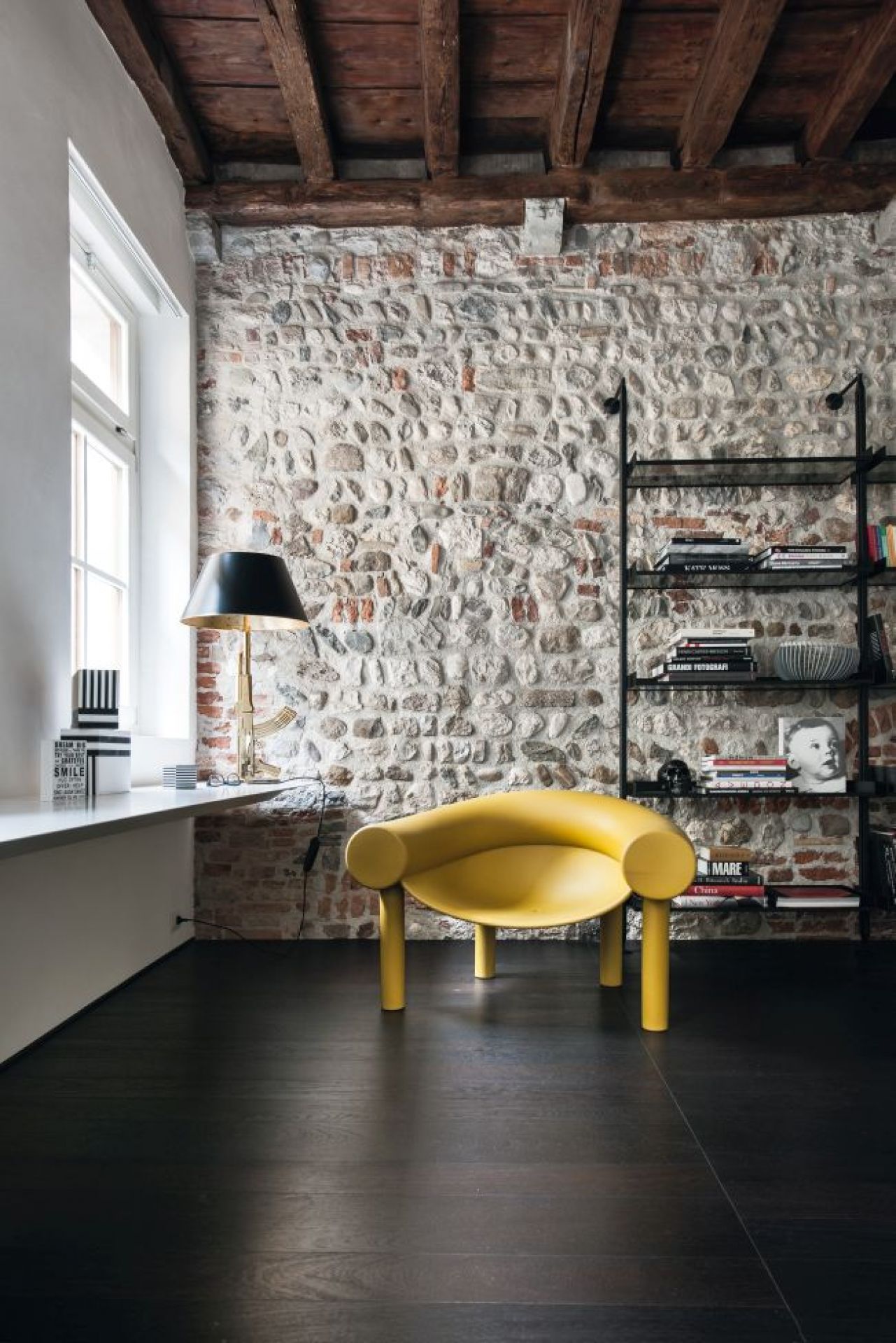 Gelber Sam Son Lounge Sessel von Magis vor einer Steinwand und Bücherregal.
