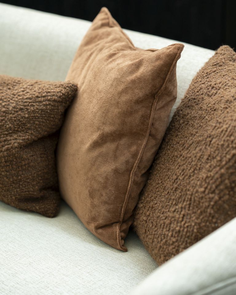 Nahaufnahme von drei braunen Zierkissen, darunter ein Ethnicraft Wave Cushion Kissen, auf einem hellen Sofa.