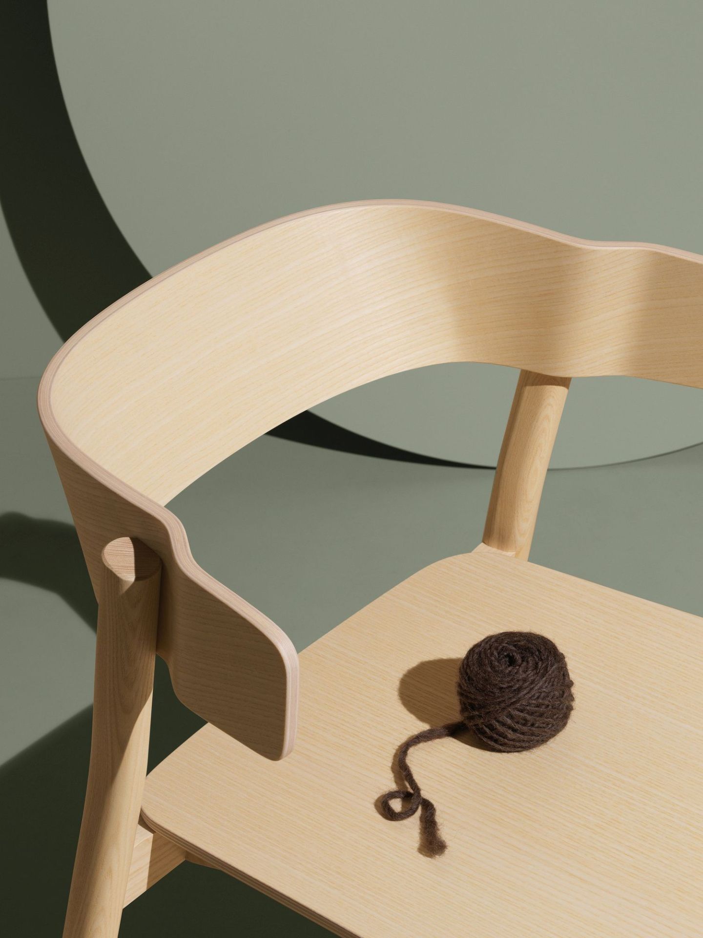 Detailaufnahme des hellen Holzstuhls Enfold Chair von Mizetto mit braunem Wollknäuel auf der Sitzfläche.