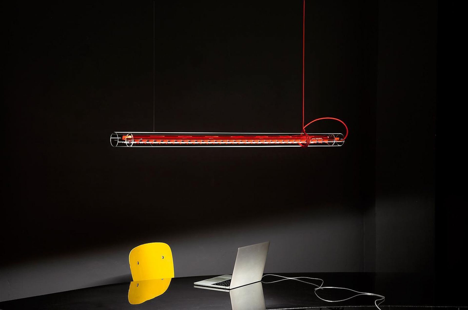 Nahaufnahme der Tubular LED Hängeleuchte von Ingo Maurer mit rotem Kabel über einem Schreibtisch.