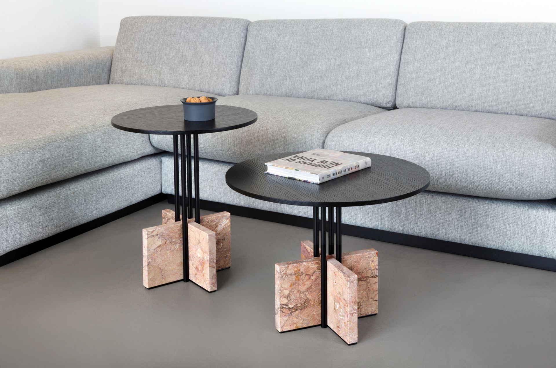 Zwei Gravity Table Beistelltische Favius mit schwarzer Tischplatte und Marmorfuß neben einem grauen Sofa.