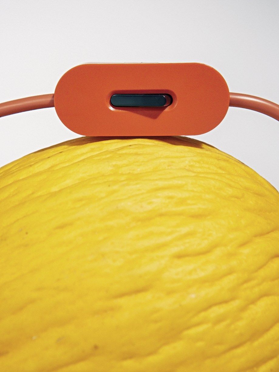 Detailaufnahme der Bilboquet Tischleuchte von Flos in Leinenoptik, mit orangefarbenem Schalter auf gelbem Hintergrund.