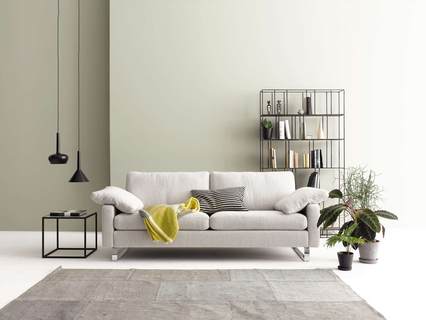 Helles Conseta Sofa mit Kissen und Decke im Wohnzimmer, neben Regal und Beistelltisch.