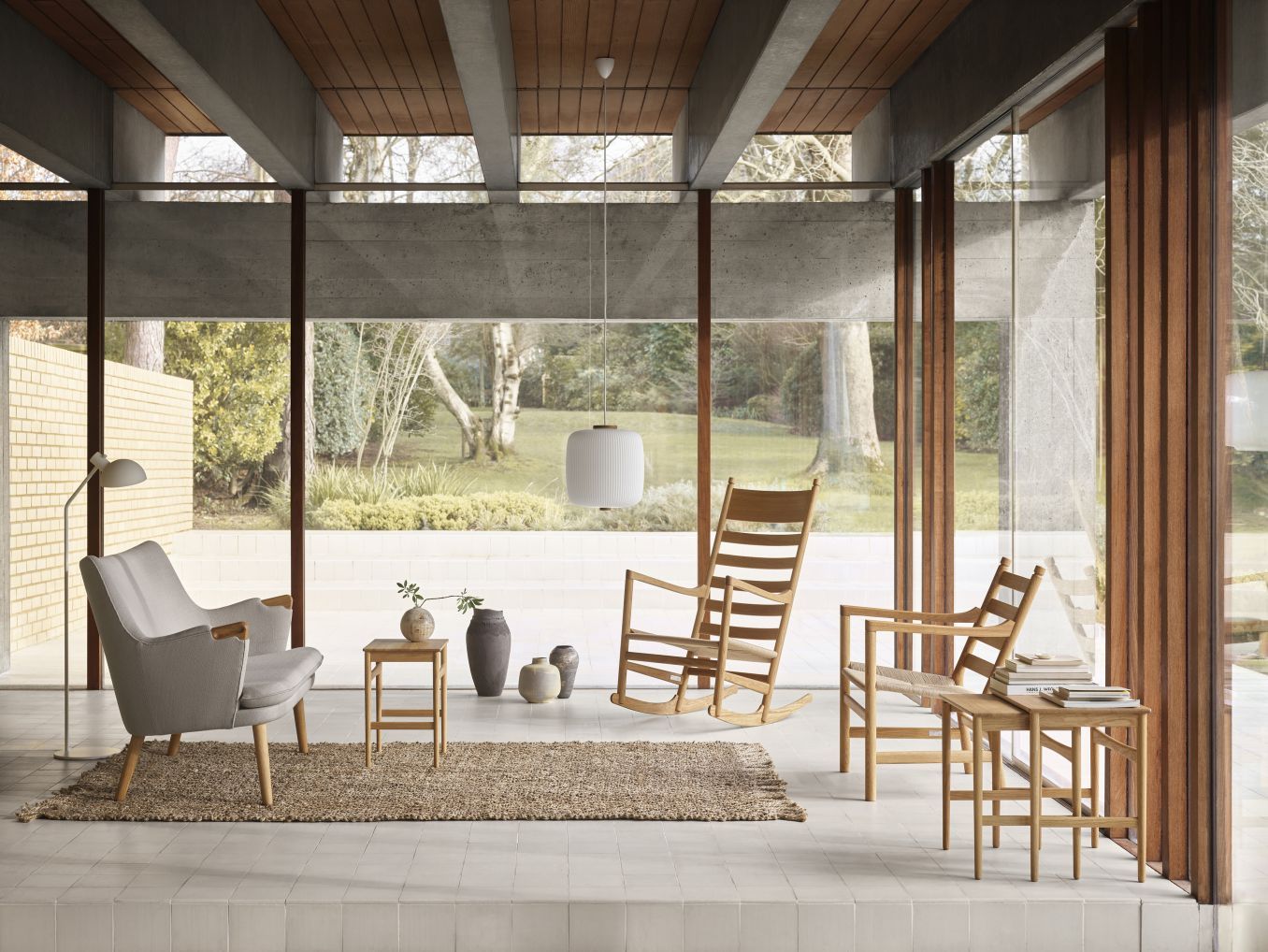 Helles Wohnzimmer mit CH45 Schaukelstuhl von Carl Hansen, Sessel, Beistelltischen und Teppich vor Fensterfront.