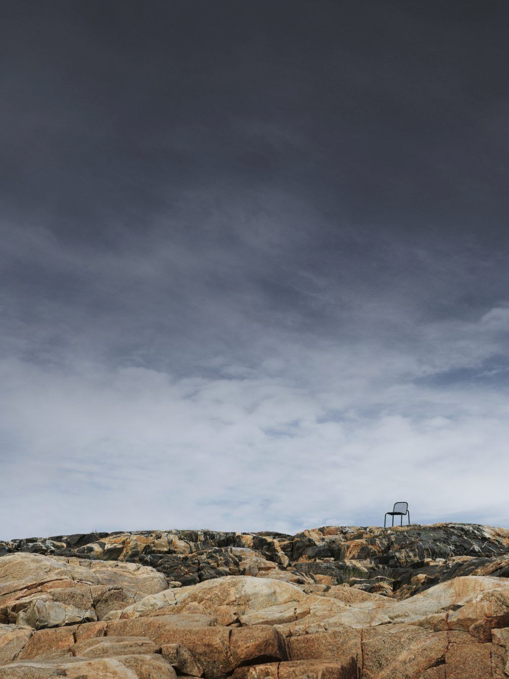 Vig Chair Stuhl von Normann Copenhagen auf Felsen unter bewölktem Himmel, Outdoor Möbel.