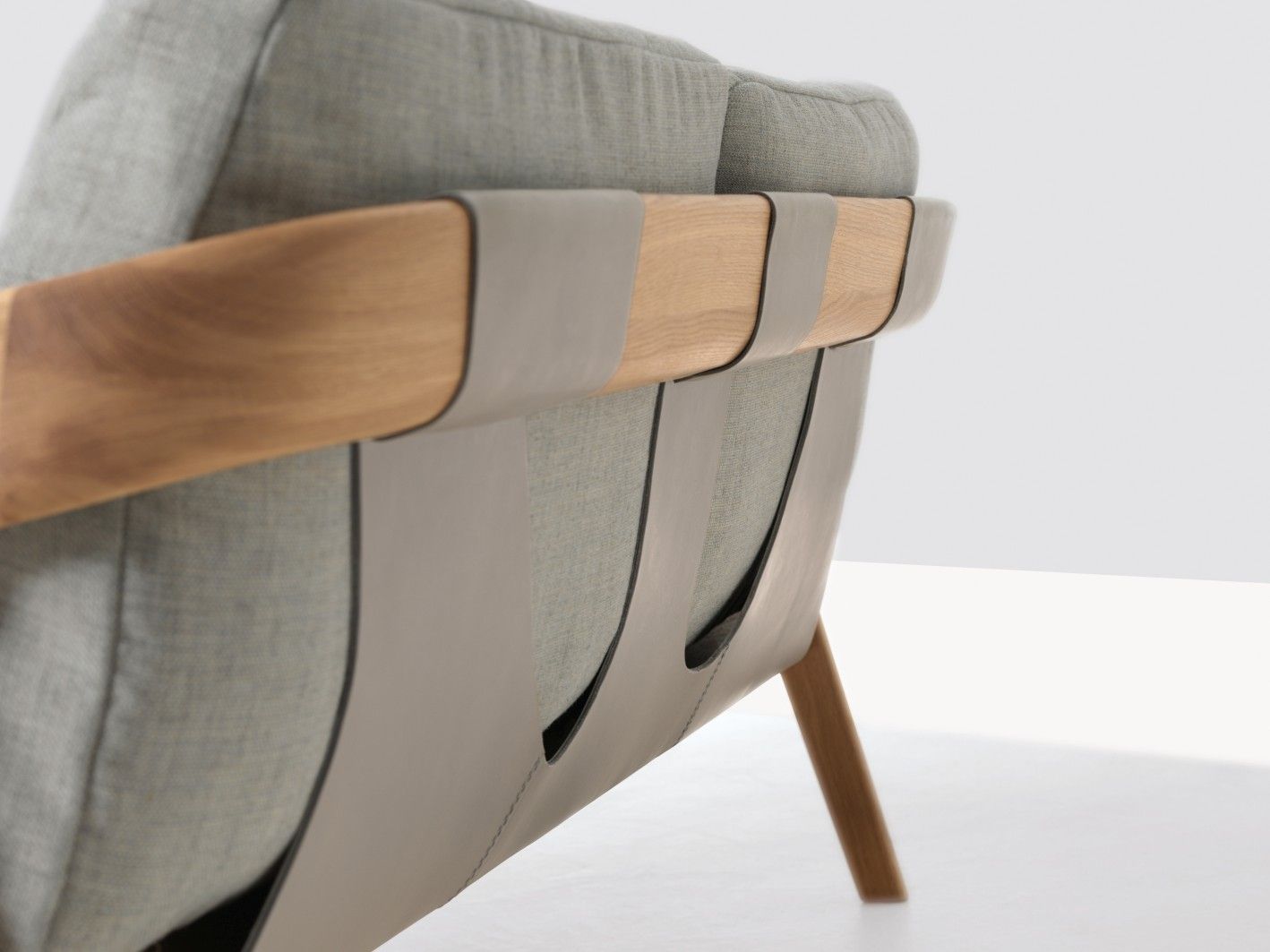Detailaufnahme des Friday 2 Sofas: Grauer Stoffbezug, Holzrahmen und Lederriemen für modernes Wohnzimmerdesign.