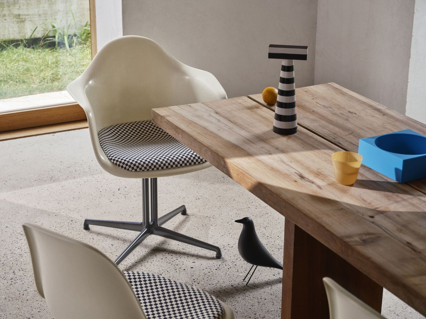 Eames Plastic Arm Chair DAL von Vitra mit Sitzpolster in Schachbrettmuster am Holztisch.