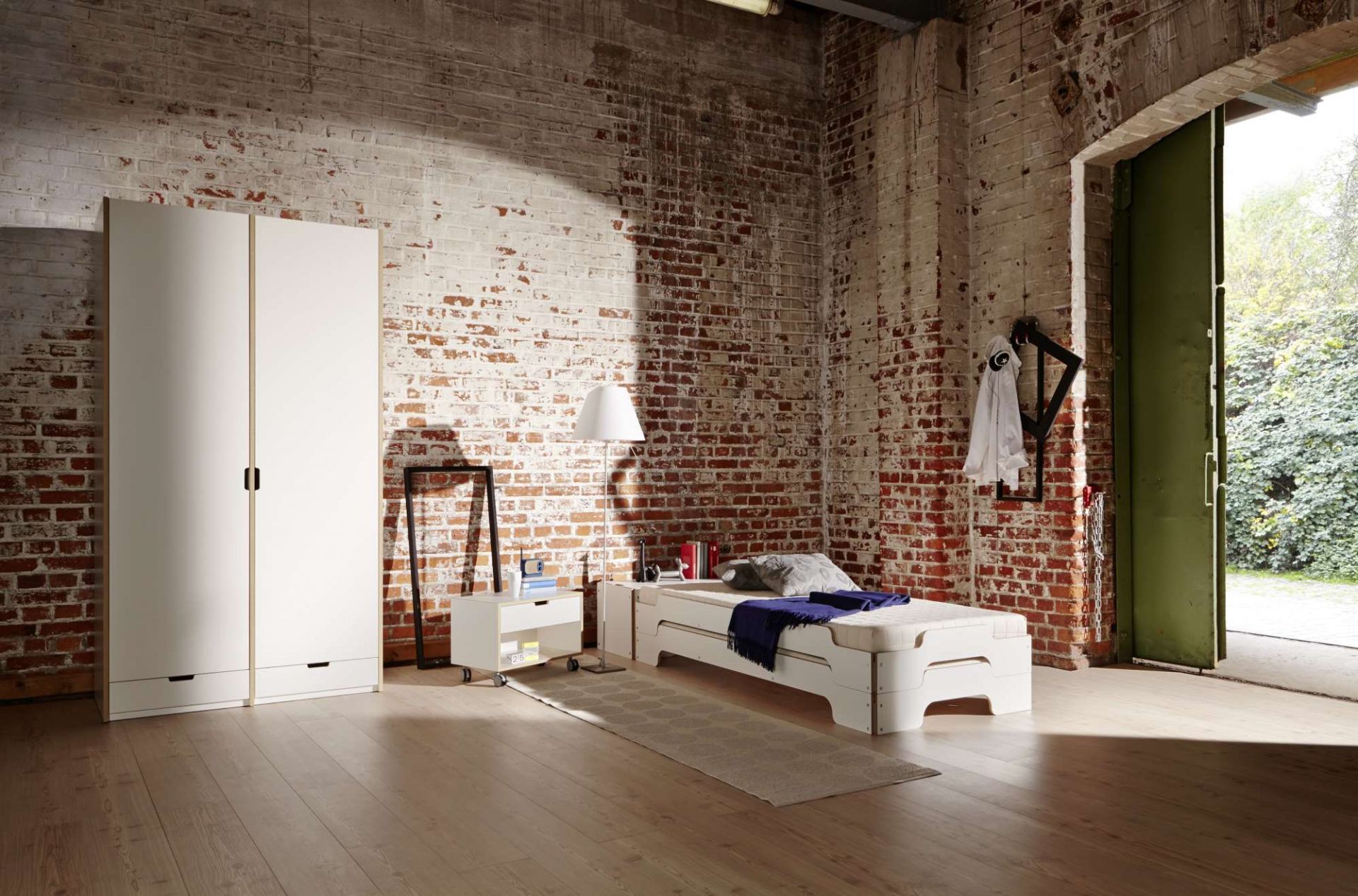 Weißes Stapelliege Bett von Müller Möbelwerkstätten mit Nachttisch und Kleiderschrank vor Backsteinwand.
