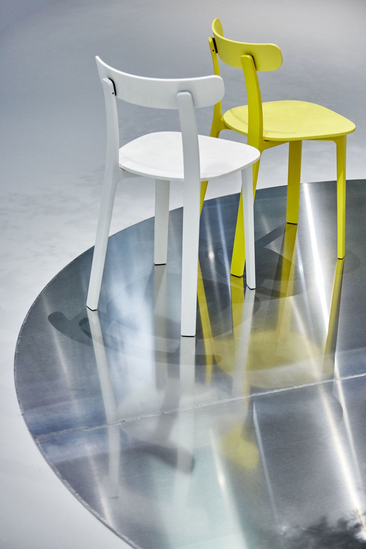 Zwei Vitra All Plastic Chairs in Weiß und Gelb auf einer runden Metallfläche.