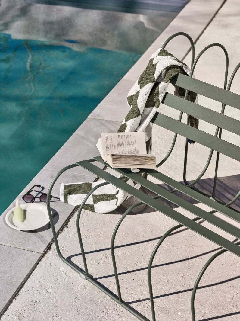 Gardener's Sofa von Design House Stockholm im Außenbereich neben Pool mit Buch, Handtuch und Sonnenbrille.