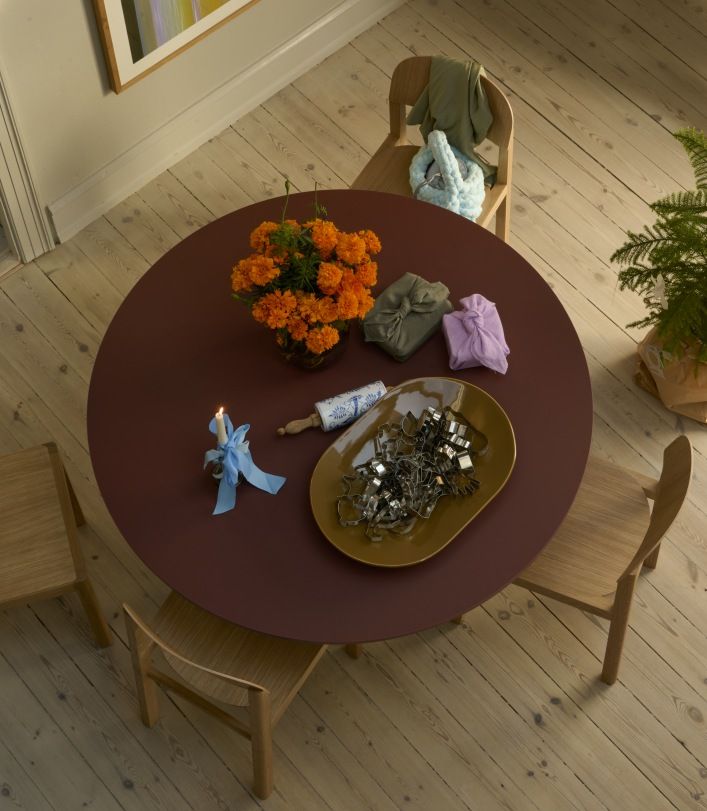 Draufsicht auf den runden, bordeauxroten Muuto MIDST Table Esstisch mit Dekoration und Holzstühlen auf hellem Holzboden.