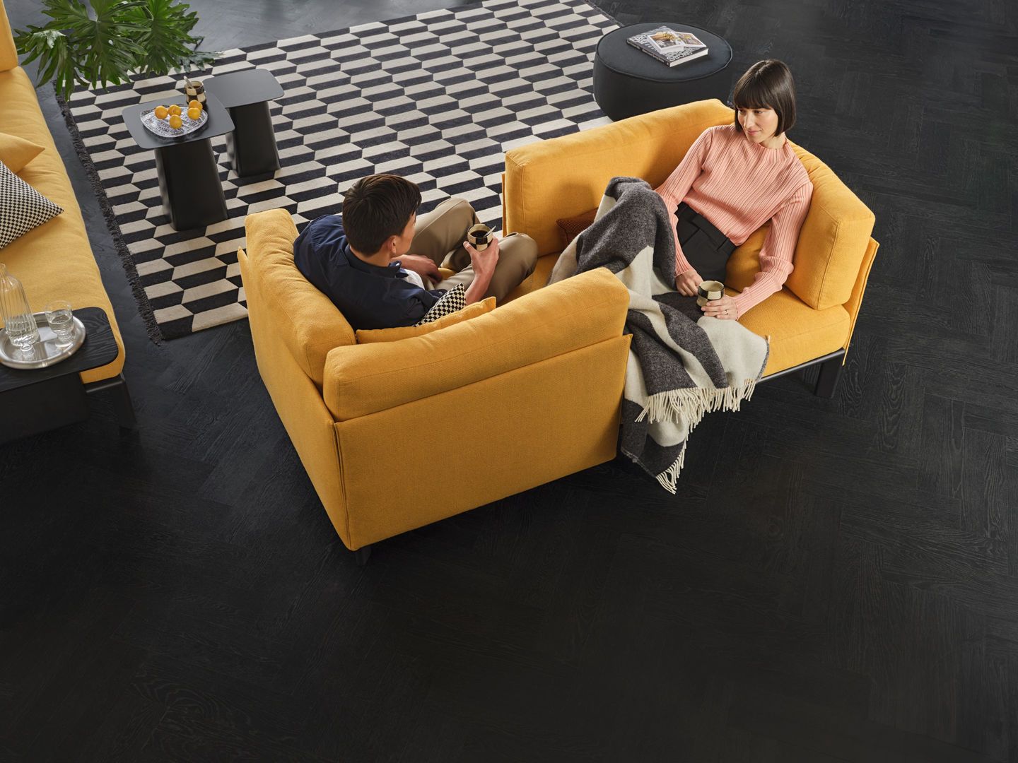 Vitra Anagram Panel 110 cm: Zwei Personen entspannen auf einem gelben Designersofa mit Decke.