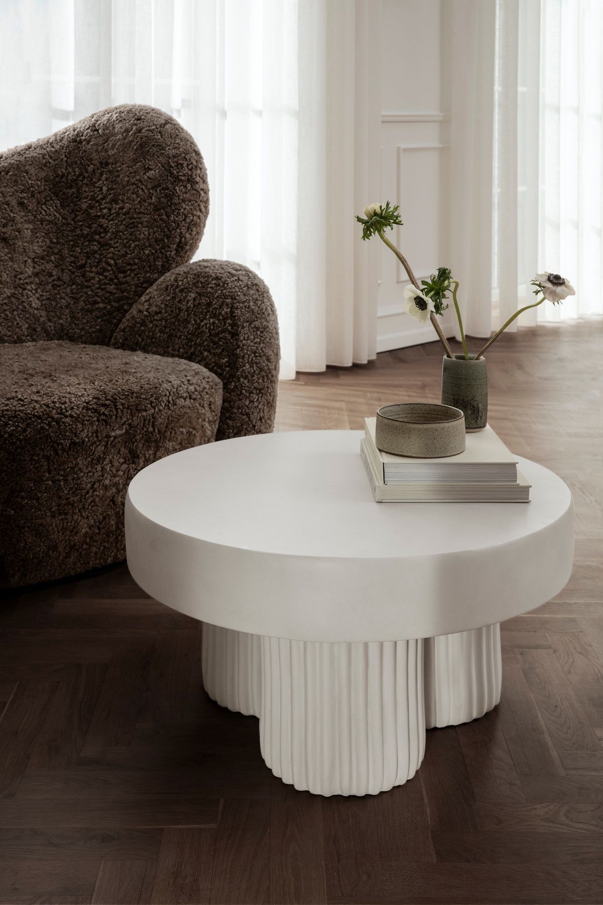 Brauner NORR11 Big Lounge Sessel aus Bouclé-Stoff neben einem runden, weißen Couchtisch mit Dekoration.
