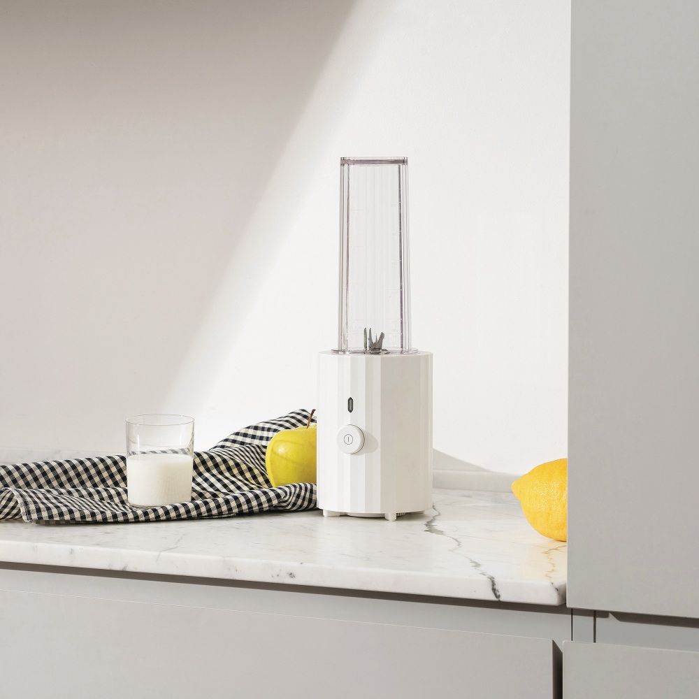Weißer Alessi Plissé Smoothie Maker auf Marmorplatte mit Zitrone und Apfel. Standmixer für gesunde Smoothies.
