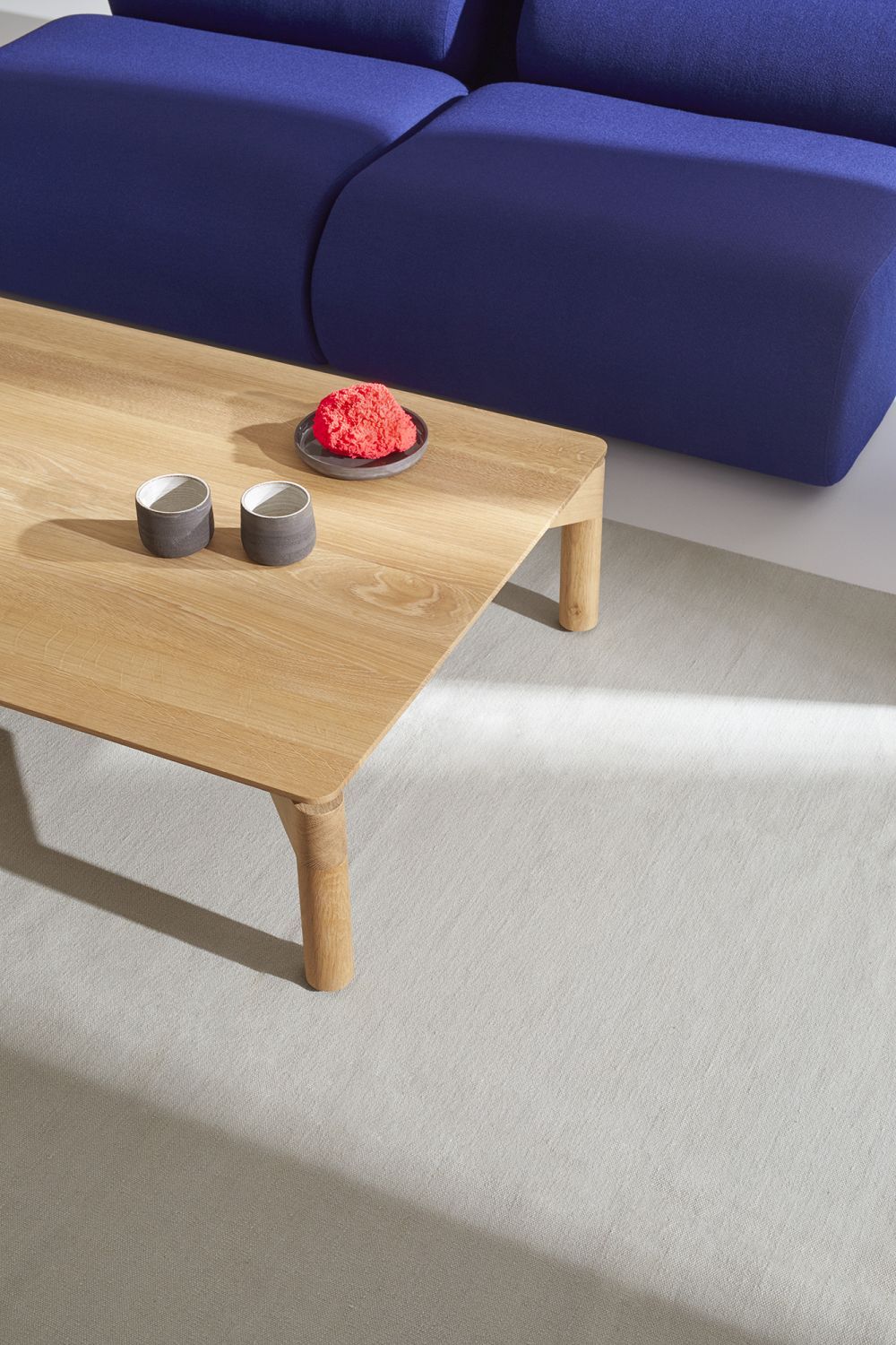 Nahaufnahme des OLA Sofas mit passendem Pouf und Holztisch mit Dekoration auf einem hellen Teppich.