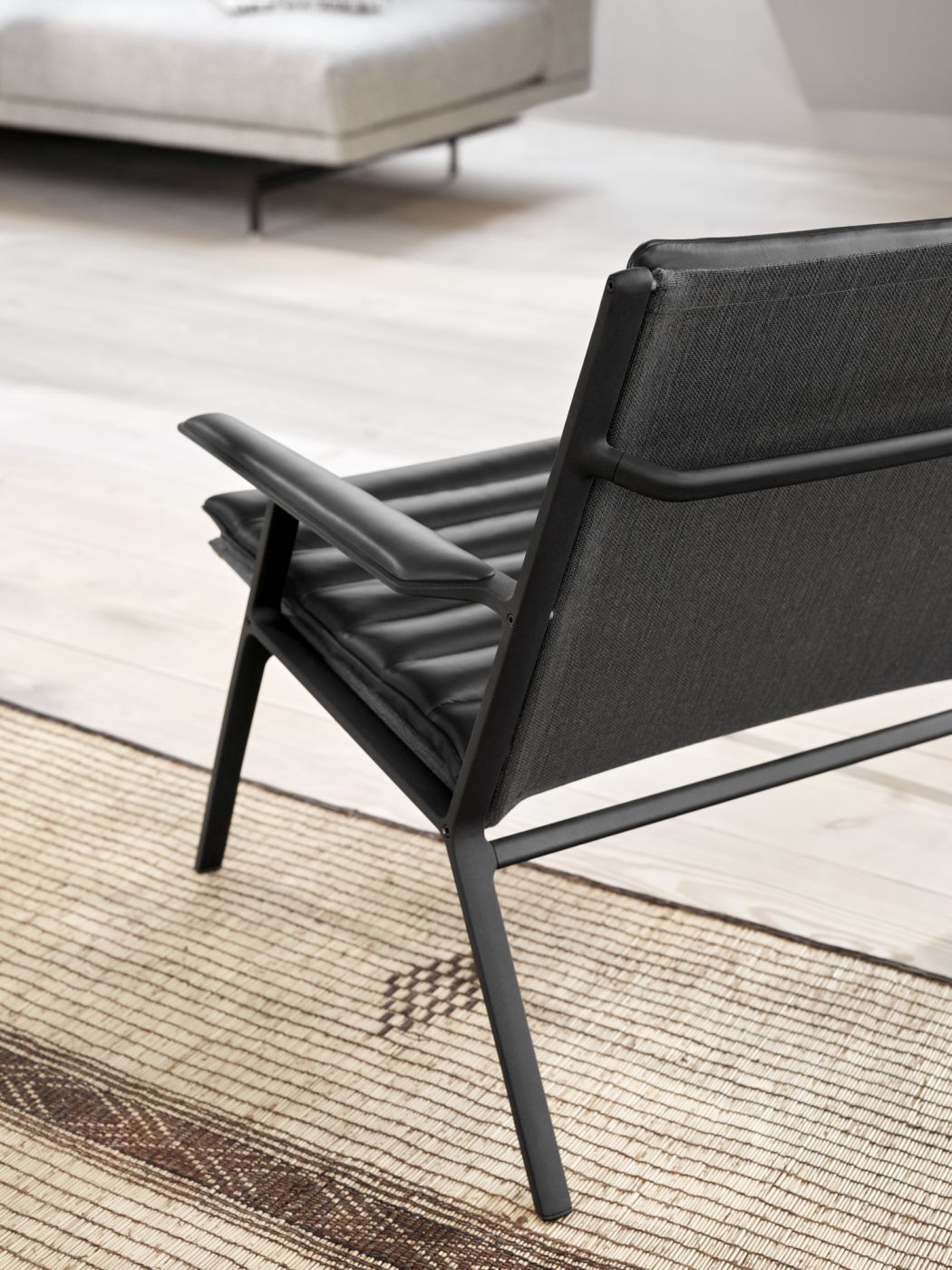 Detailaufnahme des Vipp Lounge Stuhls: Schwarzer Sessel mit Lederkissen und Textilrücken auf einem Teppich.