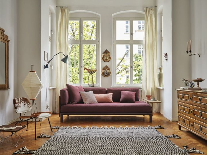 Wohnzimmer Interieur mit Vitra Anagram Panel Sofa in Weinrot, gemustertem Teppich und Designermöbeln.