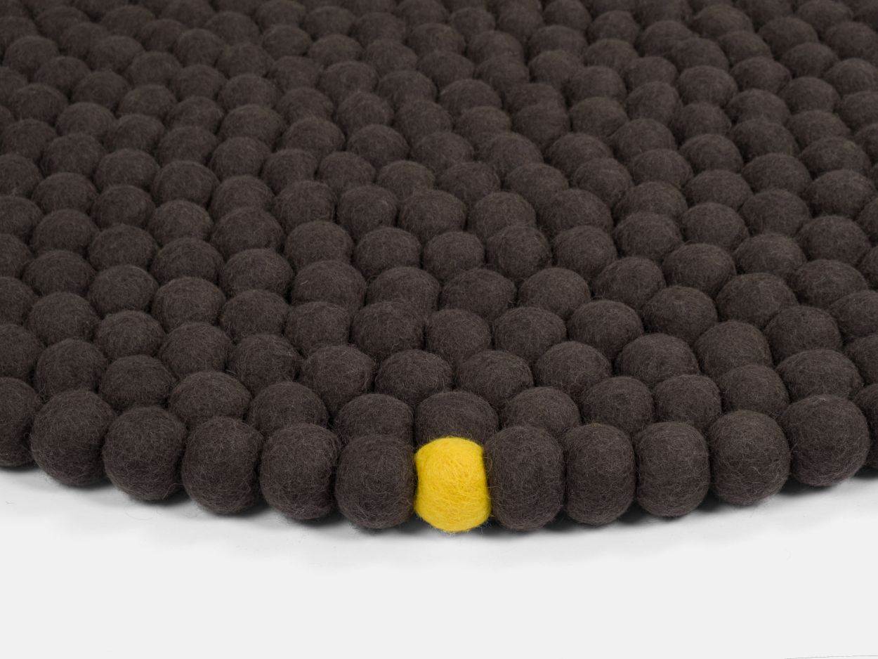 Anthrazitfarbener Filzteppich "Big One" aus Filzkugeln, Durchmesser 300 cm, mit einer gelben Filzkugel.
