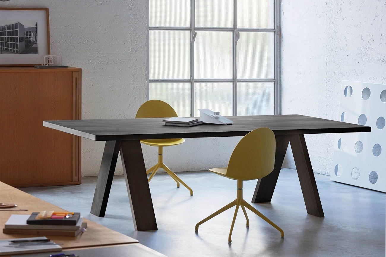 Artful Wood Table von Segis, ein dunkler Holztisch mit gelben Stühlen in einem hellen Raum.