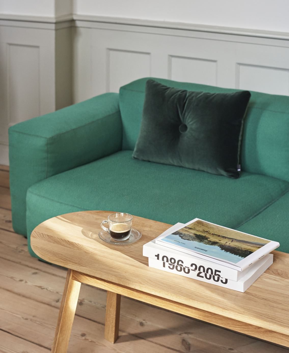 Grünes Mags Sofa mit Kissen und Holztisch mit Kaffee und Büchern im Wohnzimmer.