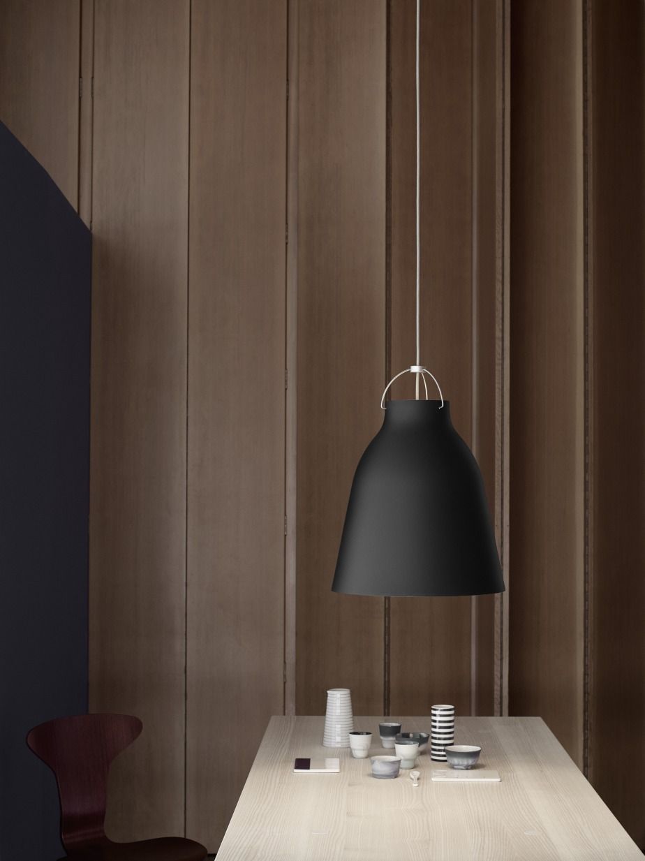 Schwarze Caravaggio Pendelleuchte von Fritz Hansen über einem Esstisch mit Geschirr vor einer Holzwand.