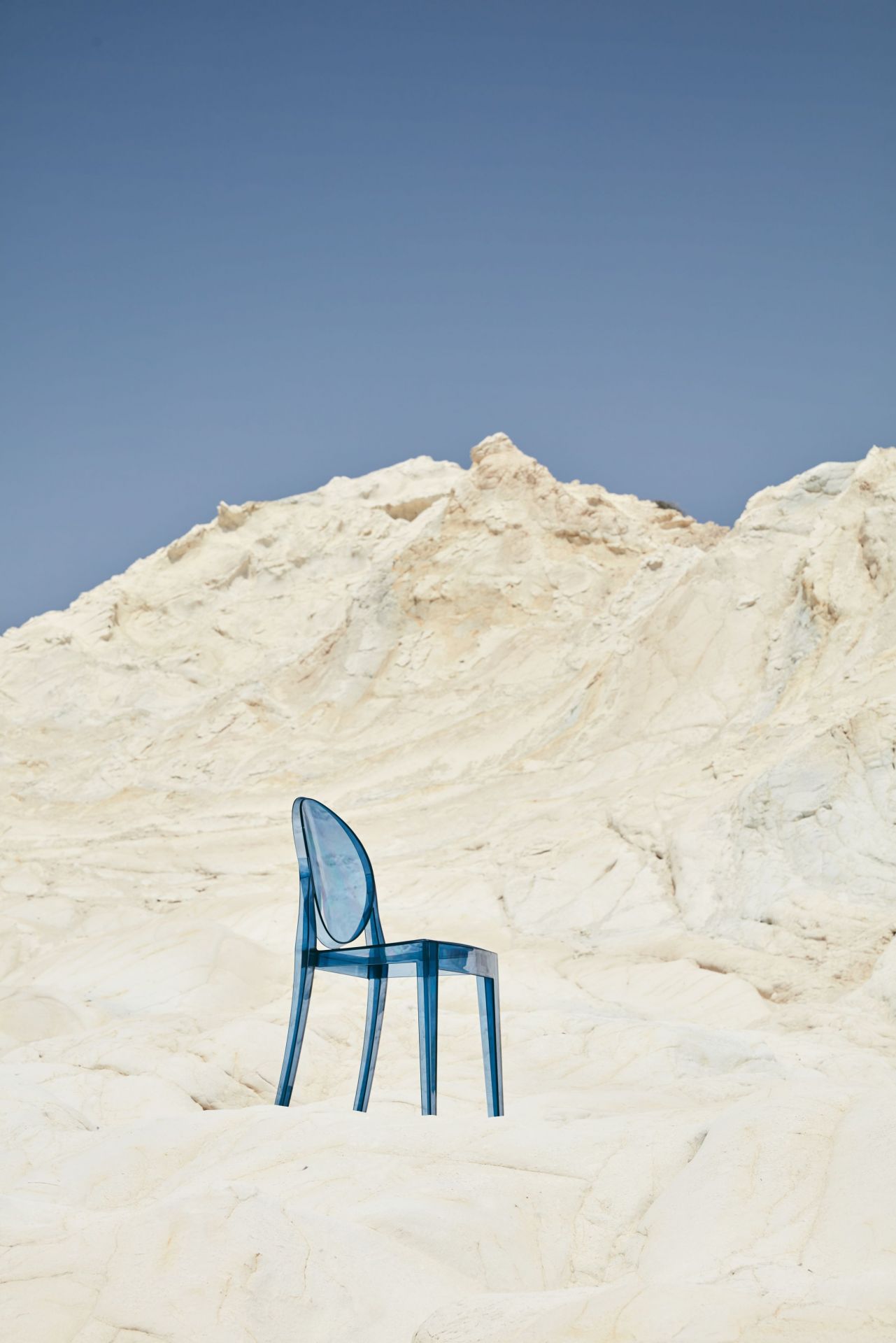 Victoria Ghost Stuhl von Kartell, glasklar, auf weißem Felsen vor blauem Himmel. Designklassiker.