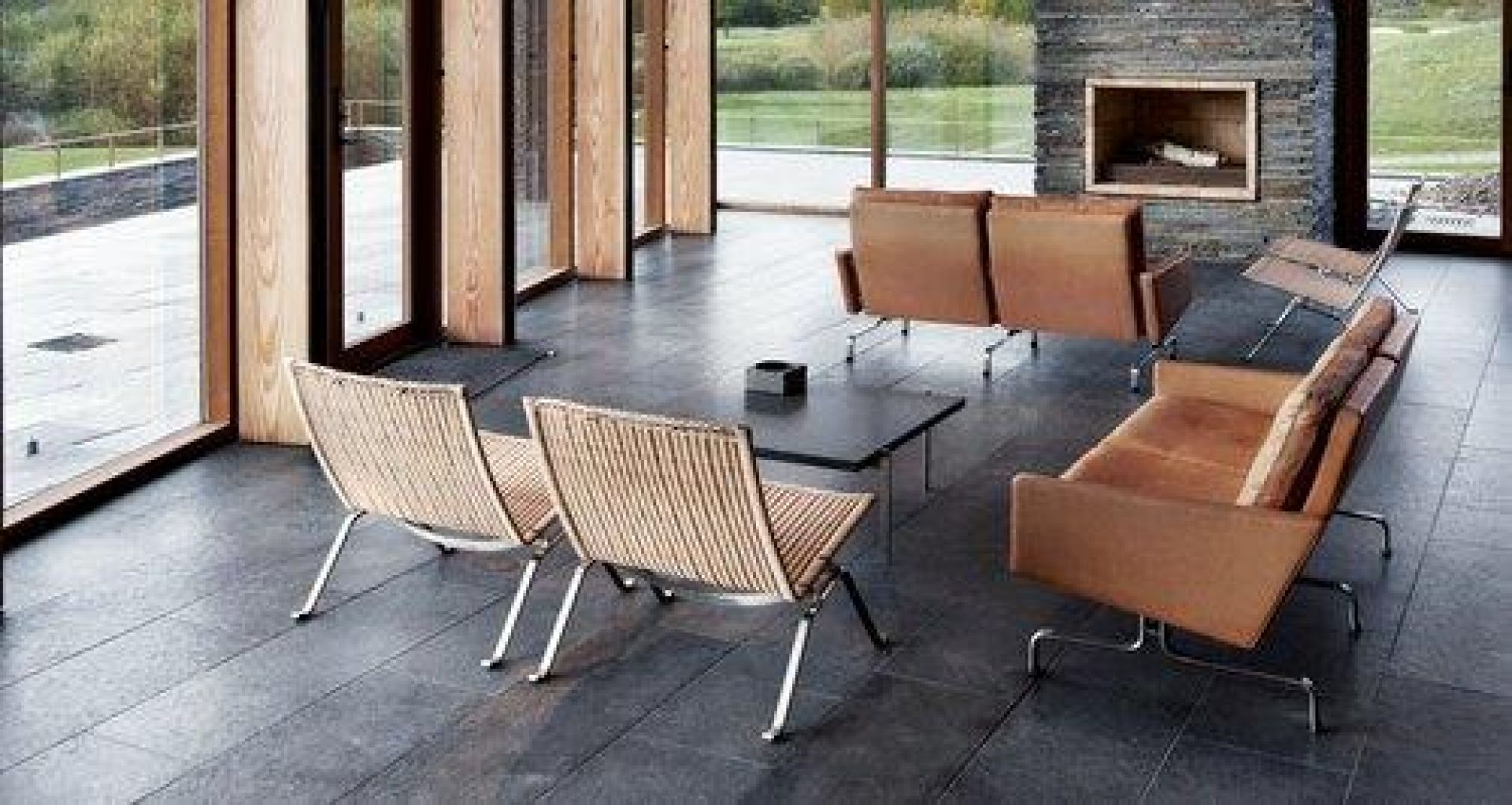 Helles Wohnzimmer mit braunem PK 31 Sofa von Fritz Hansen, Korbsesseln, Tisch und Kamin.
